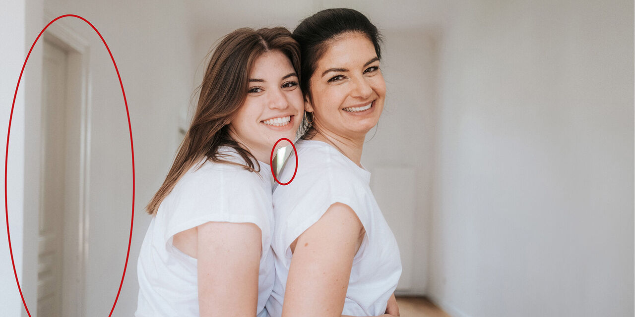 Auf dem Foto sind zwei Frauen in weißen T-Shirts zu sehen. Sie stehen in der Mitte des Bildes, aber seitlich gedreht und lächeln in die Kamera. Auf der linken Seite ist ein roter Kreis zu sehen, der eine Tür umschließt, da diese Tür ein Störfaktor auf dem Foto ist.