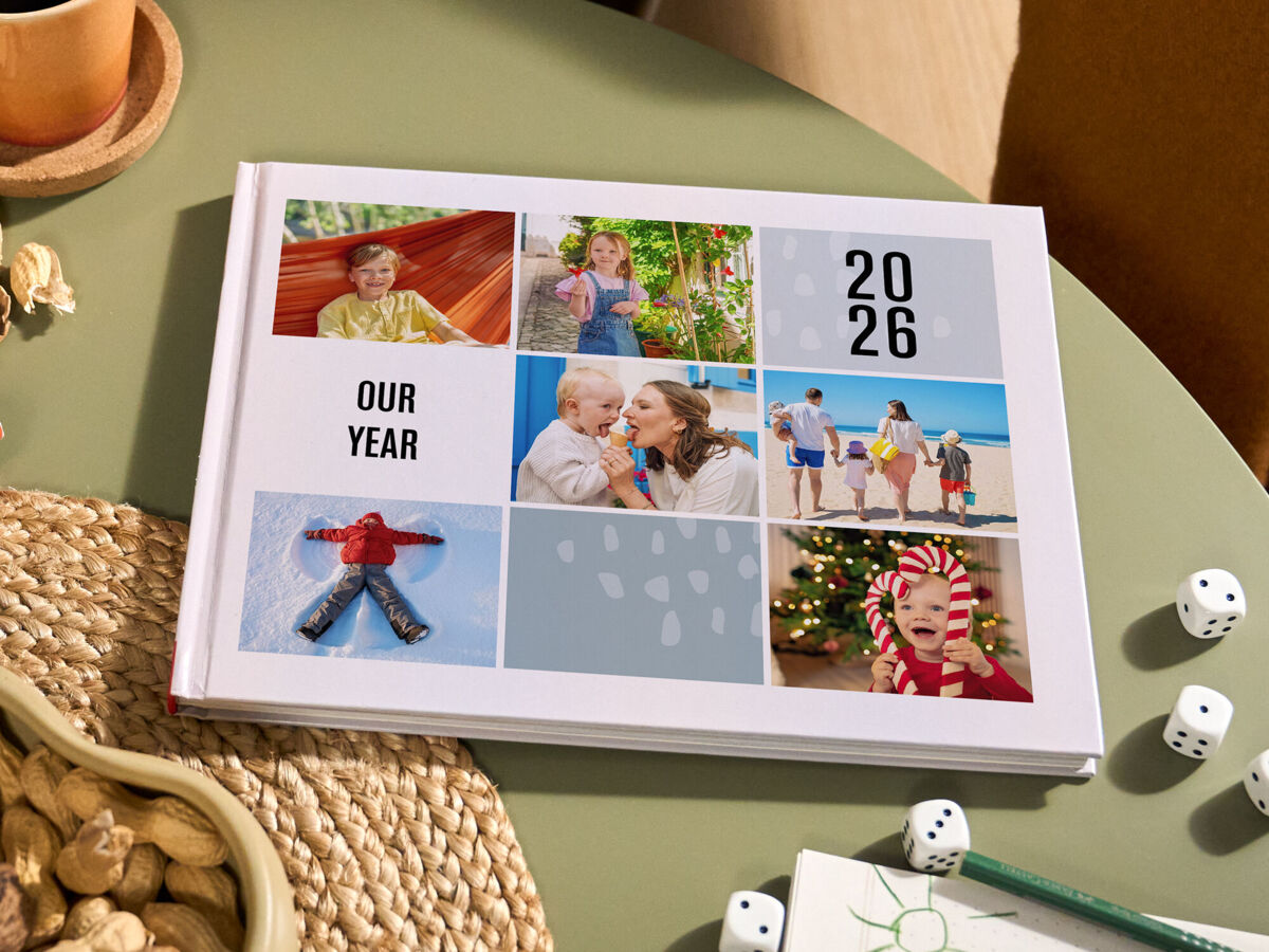 Ein weißes CEWE FOTOBUCH Cover mit einer bunten Bilder Collage einer Familie liegt auf einem runden grünen Tisch.